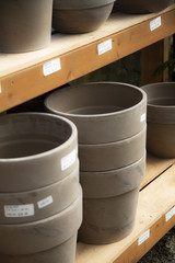 Isolated vertical view of sunlit stacks of new taupe terracotta flower pots on wooden shelves