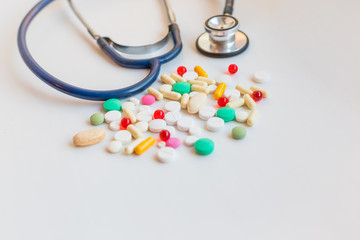 Medical theme. Stethoscope with pharmaceutical colorful pills and capsules on white background. Empty place for text. Top view. Flat design.