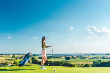 Side view of a fit woman wearing modern golf outfits, while looking at the horizon on the green...
