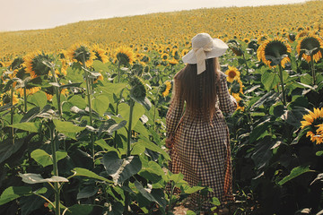 Beautiful woman in vintage boho chic dress & hat posing in rustic sunflower field