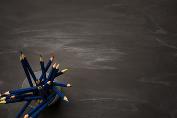 Bank container with colored pencils on black chalk Board, school background, top view, copy space