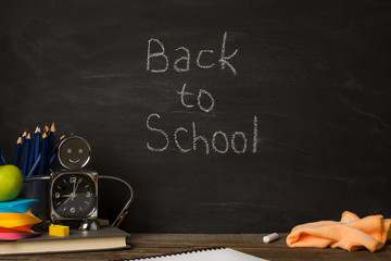 school supplies, alarm clock, pencils, chalk and rag on the table on background black chalkboard. text back to school .