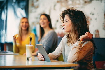 Young caucasian woman using tablet while sitting in cafe and drinking coffee.