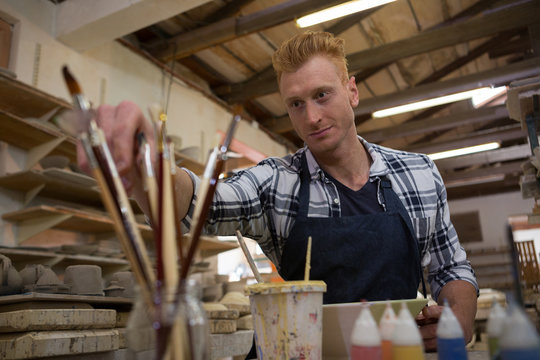 Male potter selecting a paintbrush - Powered by Adobe