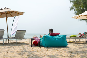 Fototapeta na wymiar Man sitting on bean bags at the beach - Summer Time