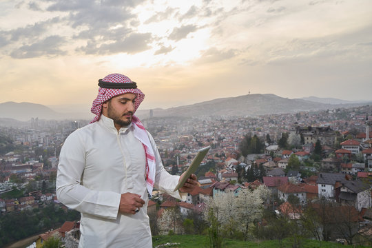 Handsome Arabic guy holding tablet. City view