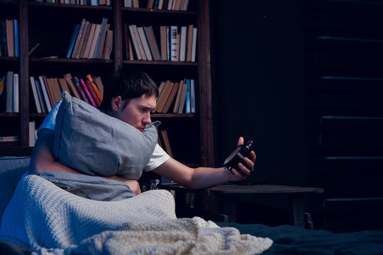 Image of man with insomnia sitting in bed with alarm clock
