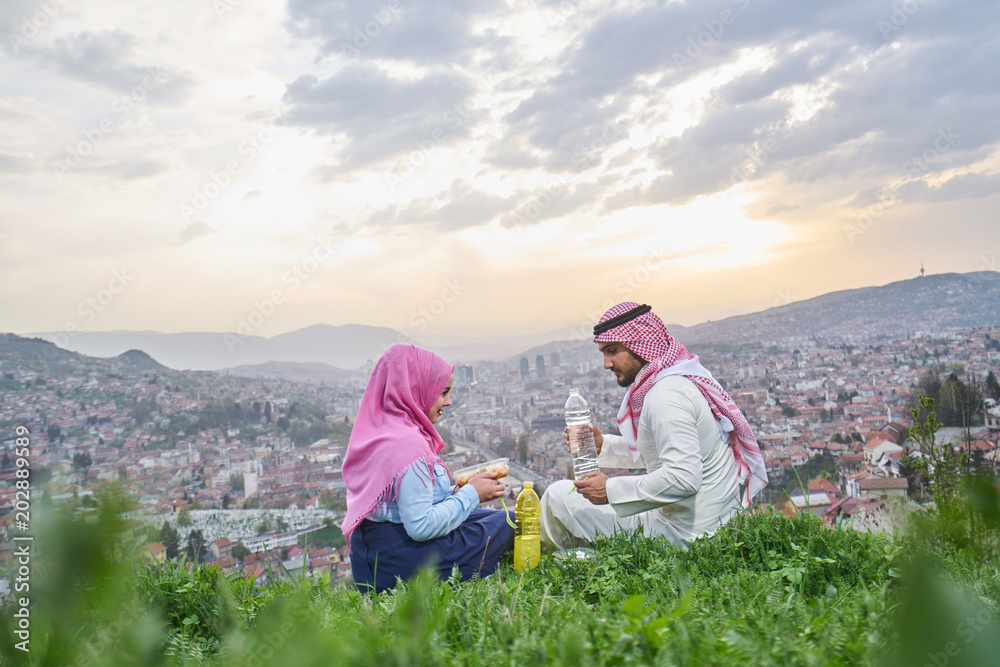 Wall mural arabic couple having a snack on the hill above a city