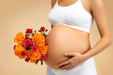 Close up of pregnant woman with bouquet of flowers on beige background. Pregnancy, maternity, preparation and expectation concept
