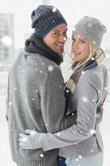 Cute couple in warm clothing hugging smiling at camera against snow falling