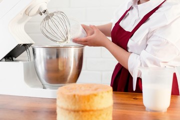 Pastry chef in red apron pours cream into cake mixer