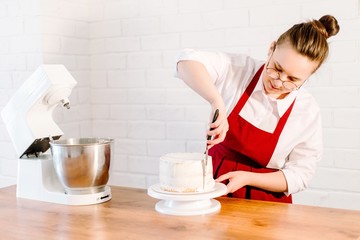 Obraz na płótnie Canvas Pastry chef in red apron bakes cake smearing white cream