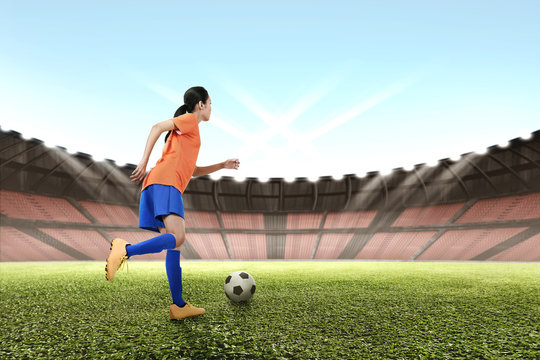 Image of asian female footballer kicking the ball