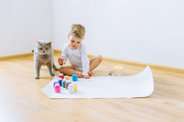 a little blond boy paints a paper with a cat