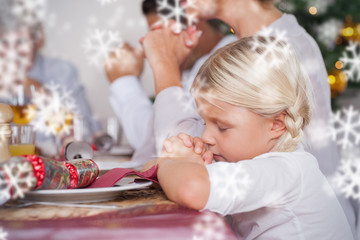 Family saying grace before dinner against snowflakes