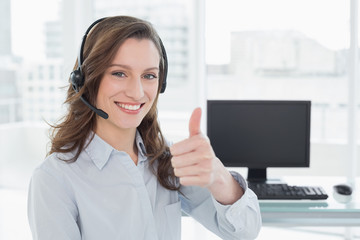 Businesswoman wearing headset while gesturing thumbs up in office