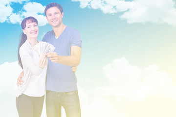 Couple holding fan of cash against blue sky