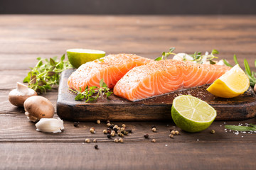 Fresh raw salmon fillet with aromatic herbs, spices on old wooden background with copy space.