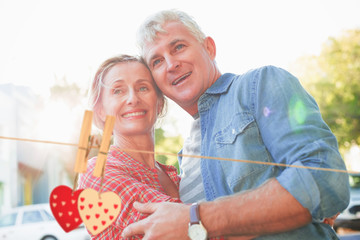 Happy mature couple hugging in the city against hearts hanging on the line