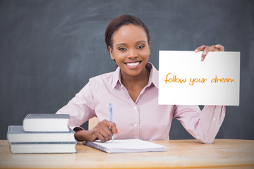 Happy teacher holding page showing follow your dreams in her classroom at school