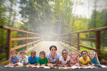 Cute pupils smiling at camera with teacher against bridge with railings leading towards forest