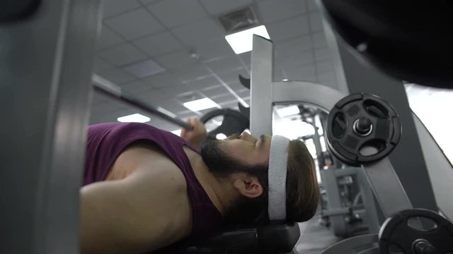 Purposeful fat man lifting gym barbell lying on bench, body workout program