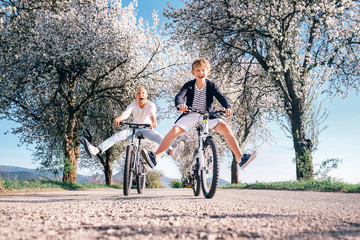 Father and son have a fun when riding bicycles on country road with blossom trees