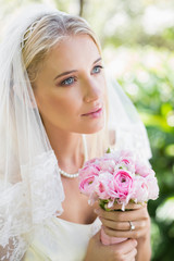 Content bride wearing veil holding bouquet looking away