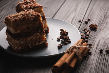 Sweet dessert tiramisu in a cut on a gray plate on a black wooden background with spices: cinnamon sticks and badan, coffee beans