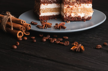 Sweet dessert tiramisu in a cut on a gray plate on a black wooden background with spices: cinnamon sticks and badan, coffee beans
