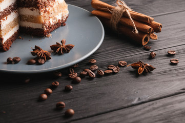 Sweet dessert tiramisu in a cut on a gray plate on a black wooden background with spices: cinnamon sticks and badan, coffee beans