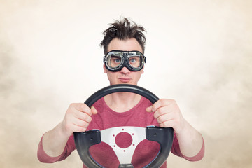 Man in stylish goggles with steering wheel on smoke background, car driver concept