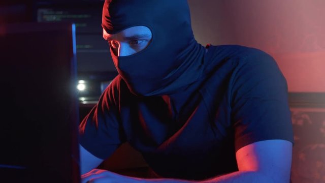 an anonymous man in a balaclava at a computer types