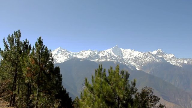 Panoramic view of Meili snow mountain range with green pine trees on foreground in Deqin, Yunnan province. Natural landscape with unique views of Himalayas