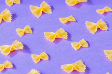 Different size of farfalle pasta on a violet background.
