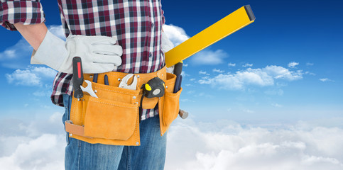 Repairman wearing tool belt while standing with hands on hips against bright blue sky with clouds