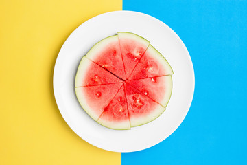 Cut watermelon on round plate with contrasting split color background.