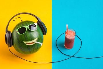 happy watermelon face listening to music and juice in glass , split color background.