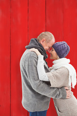 Happy mature couple in winter clothes embracing against red wooden planks