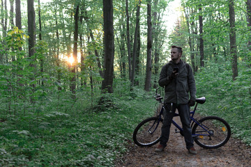 Young man with backpack and glasses standing with bicycle on the forest path of the park and looking, active lifestyle concept, sport and jorney, travel surviver concept