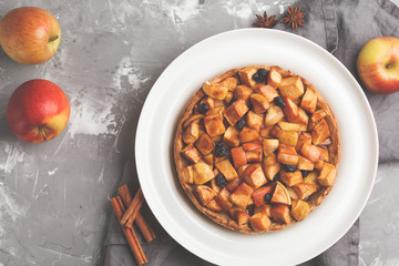 Whole vegan apple pie with cinnamon, raisins and caramel, gray background, top view