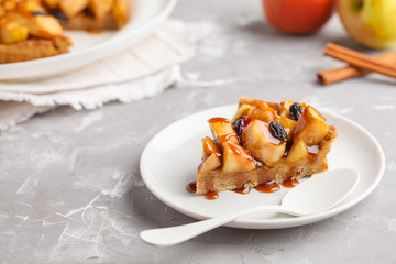 Piece of vegan apple pie with cinnamon, raisins and caramel, gray background.