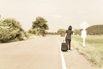 Woman with luggage hitchhiking along a road