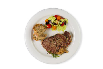 Ripened seasoned beef rump or striploin steak cooked on white plate with salad and home made bread. Top view isolated on white background.