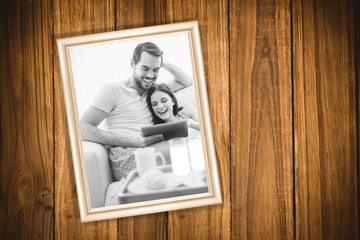Wooden background against cute couple relaxing on couch with tablet at breakfast 