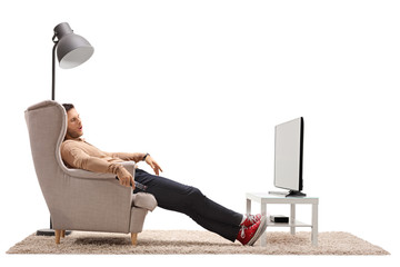 Young man sleeping in an armchair in front of a television