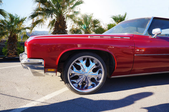 Red luxury car with chrome-plated discs against the backdrop of palm trees