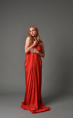 Fototapeta premium full length portrait of woman wearing red silk gown, on grey studio background.