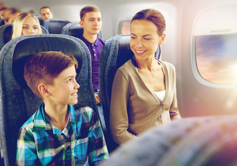 travel, tourism and family concept - happy mother and son sitting in plane and talking over...