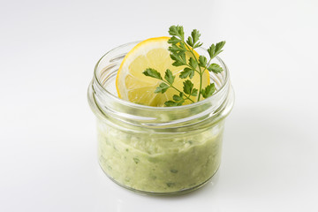 Mexican sauce guacamole in a jar with lemon slice and parsley isolated on white.